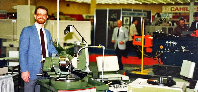 Vintage photo of a Rush Machinery representative showcasing precision grinding equipment at an industrial trade show.