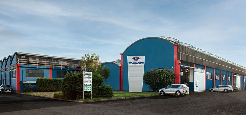 Tecnomagnete factory exterior showcasing modern facilities, with the company logo prominently displayed on the building.