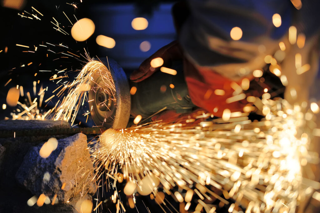 Close-up view of a metalworking process showing a grinding tool in action, producing bright, dynamic sparks as it shapes a metal surface. The image captures the intensity and precision of industrial metal fabrication